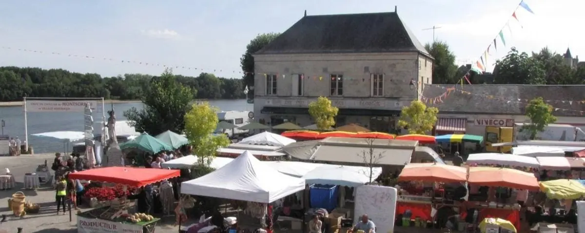 A vibrant food market in Montsoreau with colorful tents and stalls, and people shopping for fresh produce and local goods near the river.