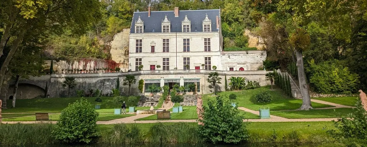 A beautiful castle surrounded by vibrant greenery, featuring a large, well-kept garden in the foreground. The white stone building stands out against the lush backdrop, showcasing its elegant architecture.
