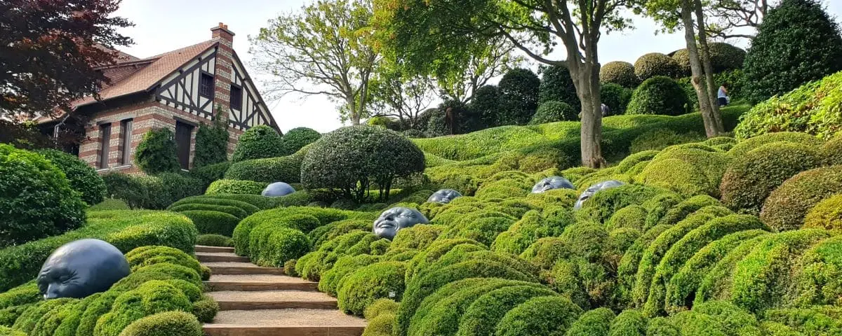 Lush garden in Etretat featuring manicured hedges, whimsical face sculptures, and a charming house with half-timbered architecture.