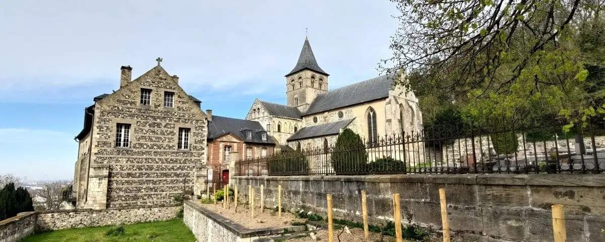 The historic Graville Abbey in Le Havre, featuring stone buildings, a church with a tall spire, and well-maintained gardens.