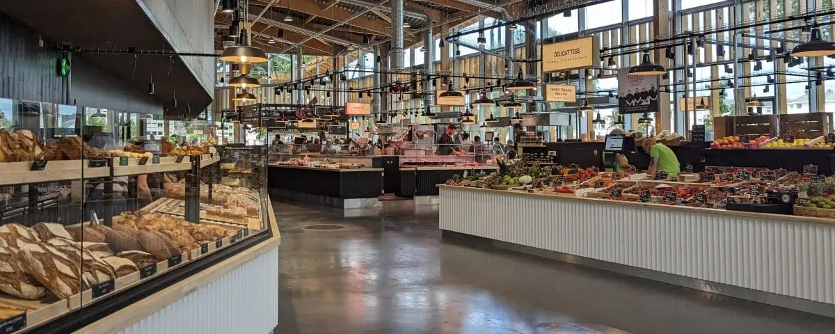 Interior of Halles Biltoki Market with various food stalls, including a bakery section with fresh bread and a produce area displaying colorful fruits and vegetables.