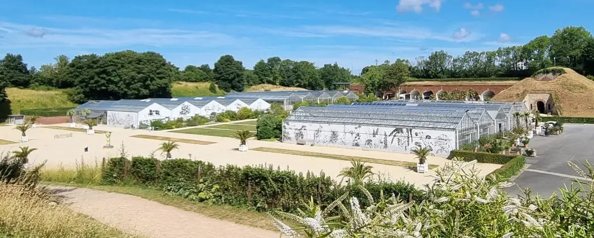 A view of the Hanging Gardens in Le Havre, showing greenhouses, well-manicured pathways, and lush vegetation under a clear blue sky.