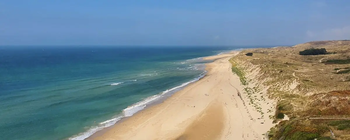 Expansive sandy beach bordered by sand dunes and clear, blue waters, showcasing the natural beauty of Hatainville Dunes.