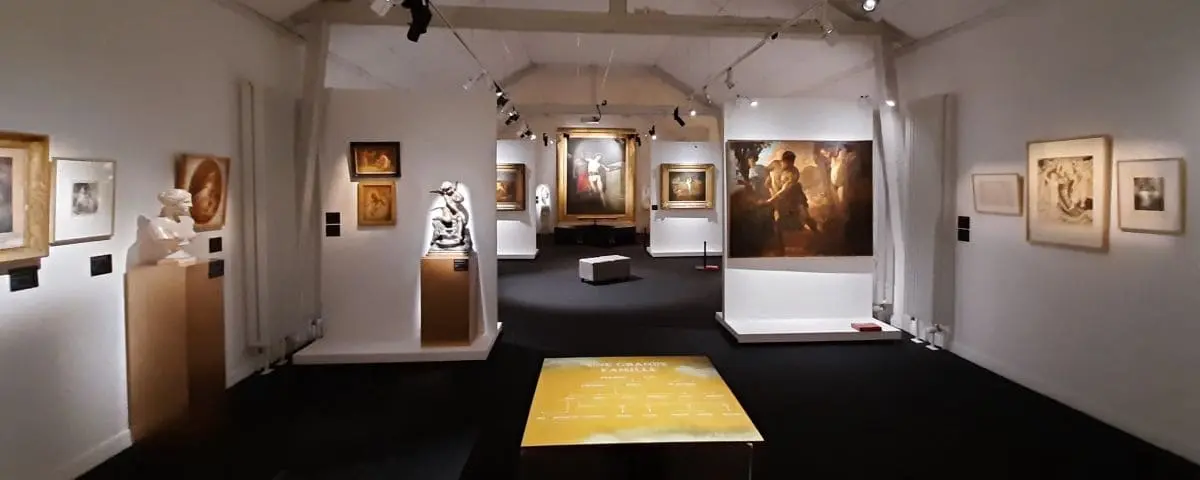 An interior view of the History Museum in Lisieux, featuring an exhibit of various artworks and sculptures displayed in a well-lit gallery. The walls are adorned with paintings, and spotlights highlight individual pieces.