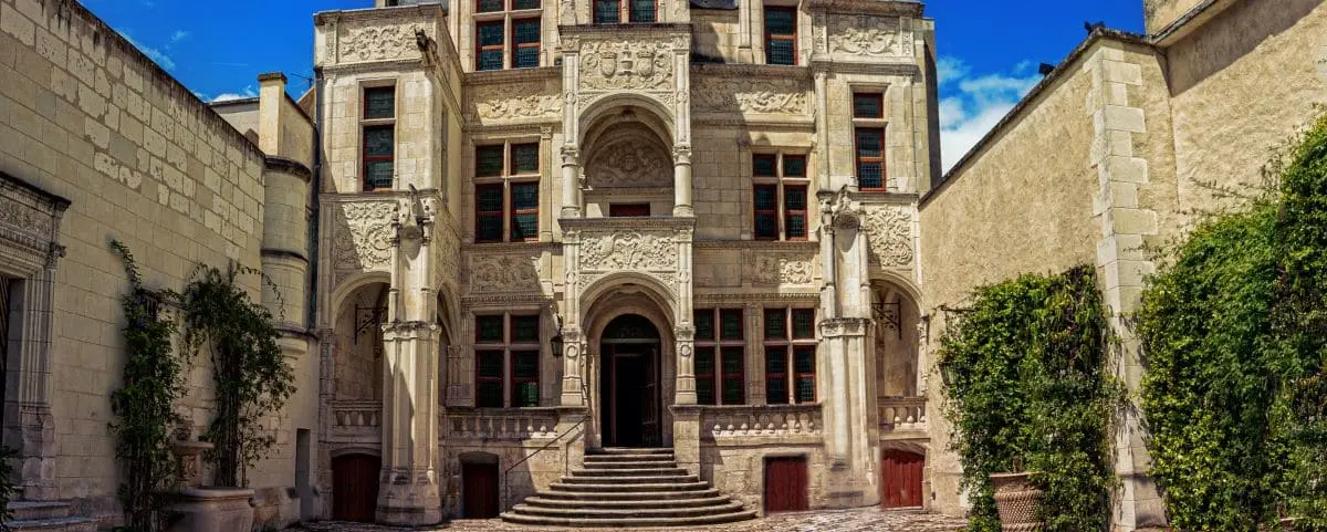 The ornate exterior of Hotel Gouin in Tours, France, showcasing detailed stone carvings and an arched entrance, with a sunny blue sky in the background.