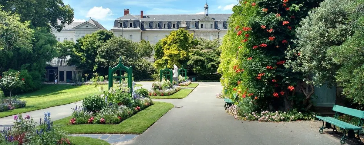 Scenic view of Jardin des Plantes with lush greenery, vibrant flowerbeds, and a historic building in the background.