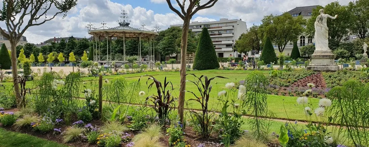 Picturesque Jardin du Mail featuring manicured lawns, ornamental trees, and a decorative pavilion, with a backdrop of city buildings.