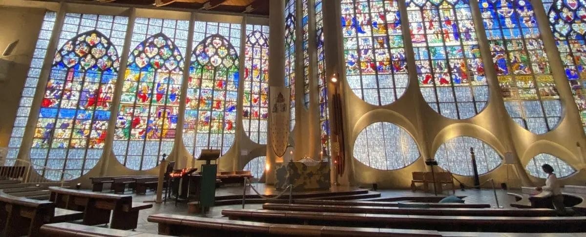 The interior of the modern Joan of Arc Church in Rouen, showcasing its stunning stained glass windows depicting colorful biblical scenes and the simple wooden pews and altar.