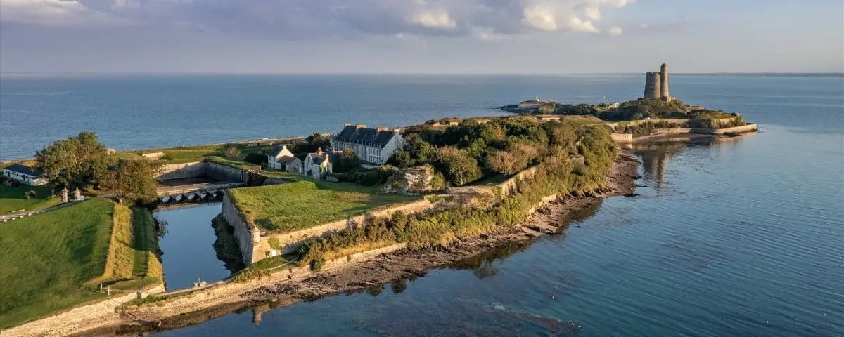 Aerial view of La Hougue, featuring a coastal landscape with a historic fortification surrounded by water.