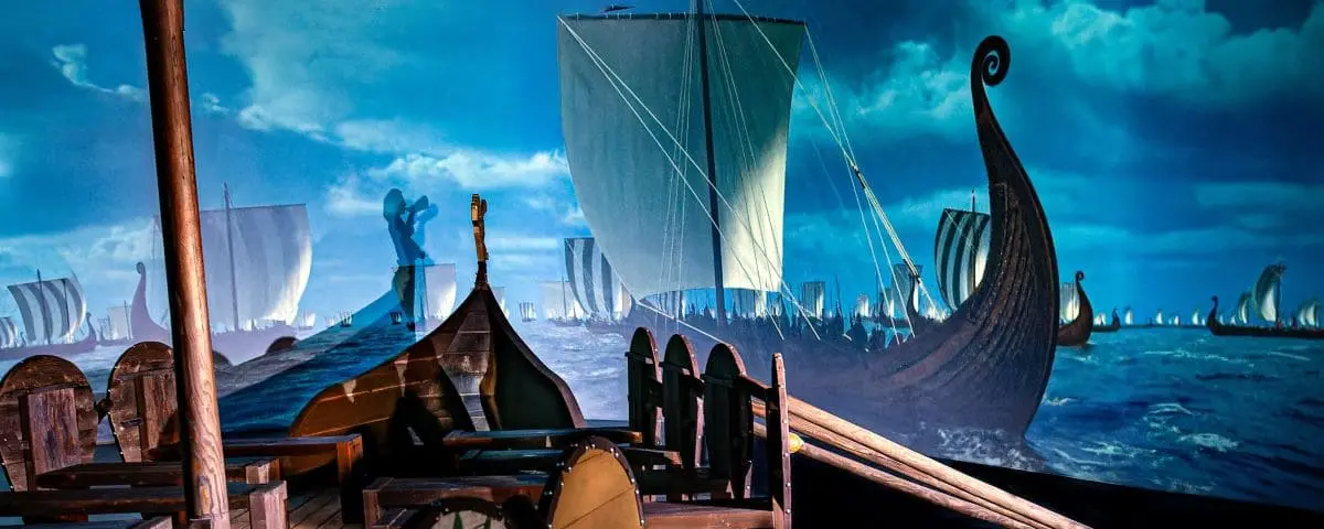 A dramatic museum exhibit depicting Viking ships at sea, with a backdrop of a stormy ocean and cloudy sky. The display includes wooden ship models and creates an immersive, historical atmosphere.