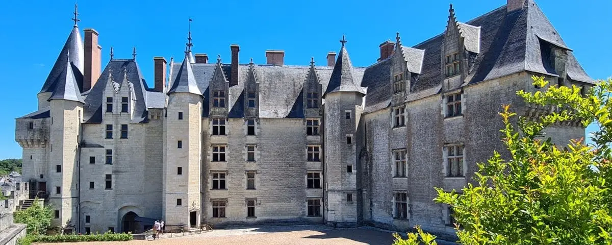 Front view of Langeais Castle showcasing its medieval architecture with numerous turrets and fortified walls, with visitors visible at the entrance.