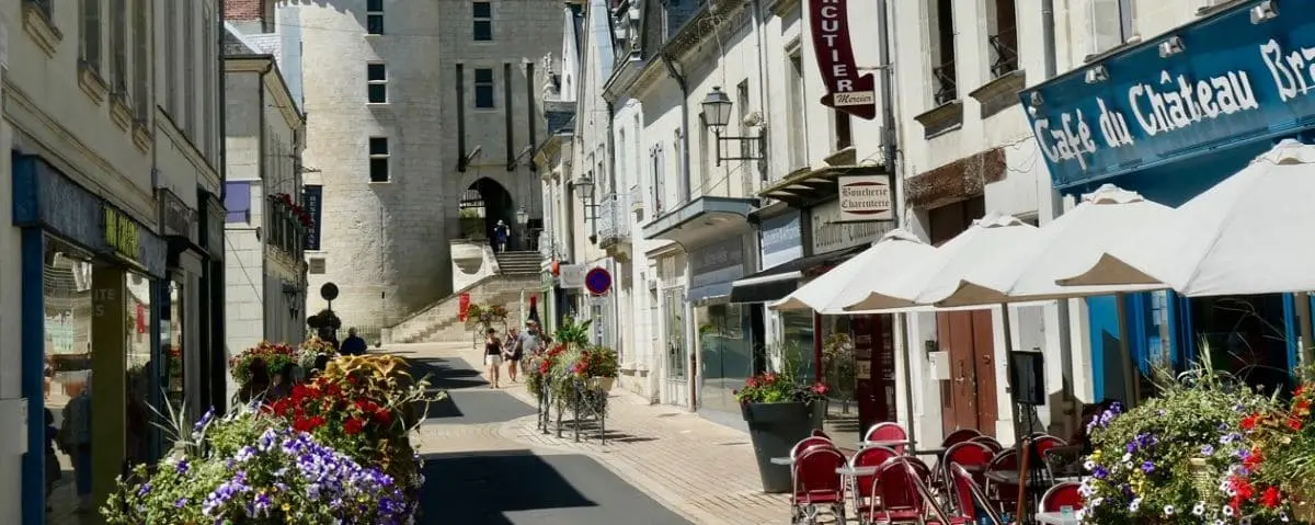 Picturesque street in the town center of Langeais with colorful flowers, outdoor cafes, and historic buildings lining the street leading up to a castle entrance.