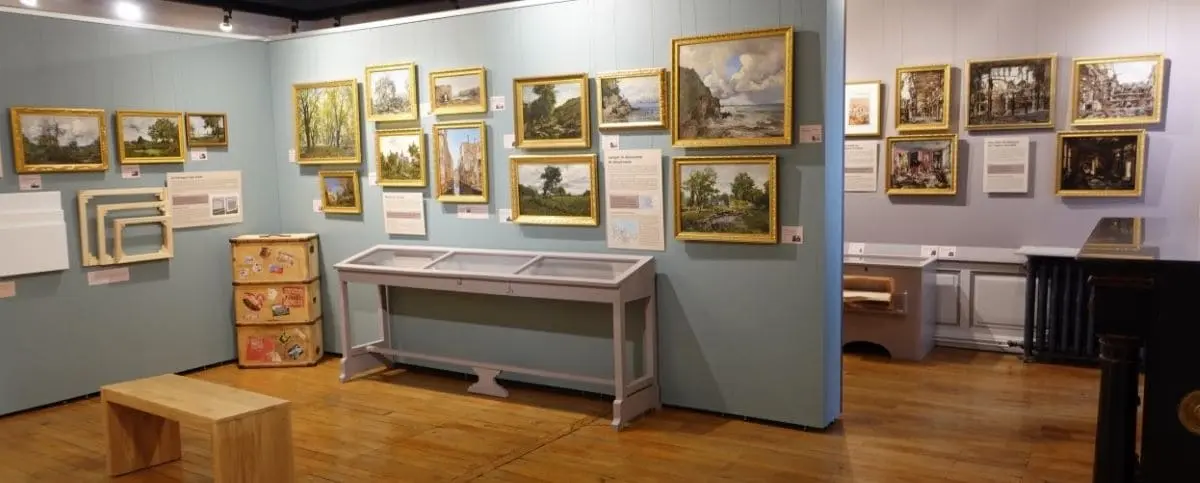 An art exhibition room at the Lansyer Museum in Loches. The walls are adorned with framed paintings, and there are display cases and informational panels.