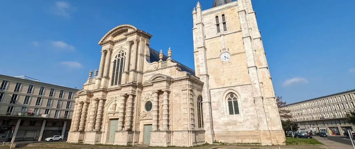The exterior of Le Havre Cathedral, showcasing its grand architectural design with a prominent clock tower and intricate details under a clear blue sky.