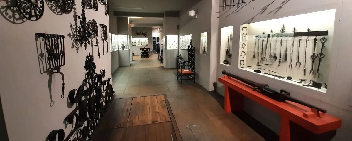An exhibit in the Le Secq des Tournelles Museum, displaying intricate wrought ironwork, including gates and various tools, within a long, narrow gallery.