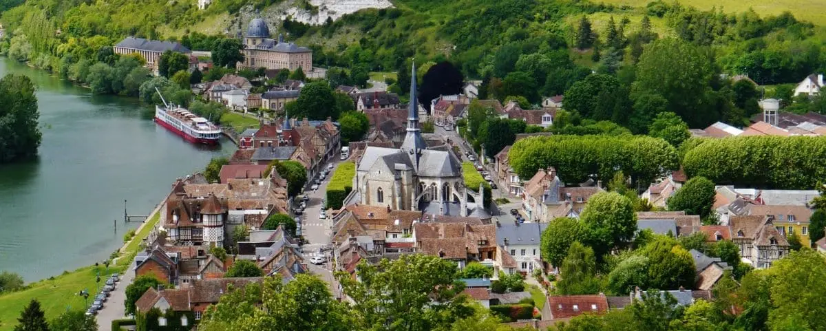 Picturesque town of Les Andelys nestled along a river with historic buildings, a central church, and lush greenery surrounding the area.