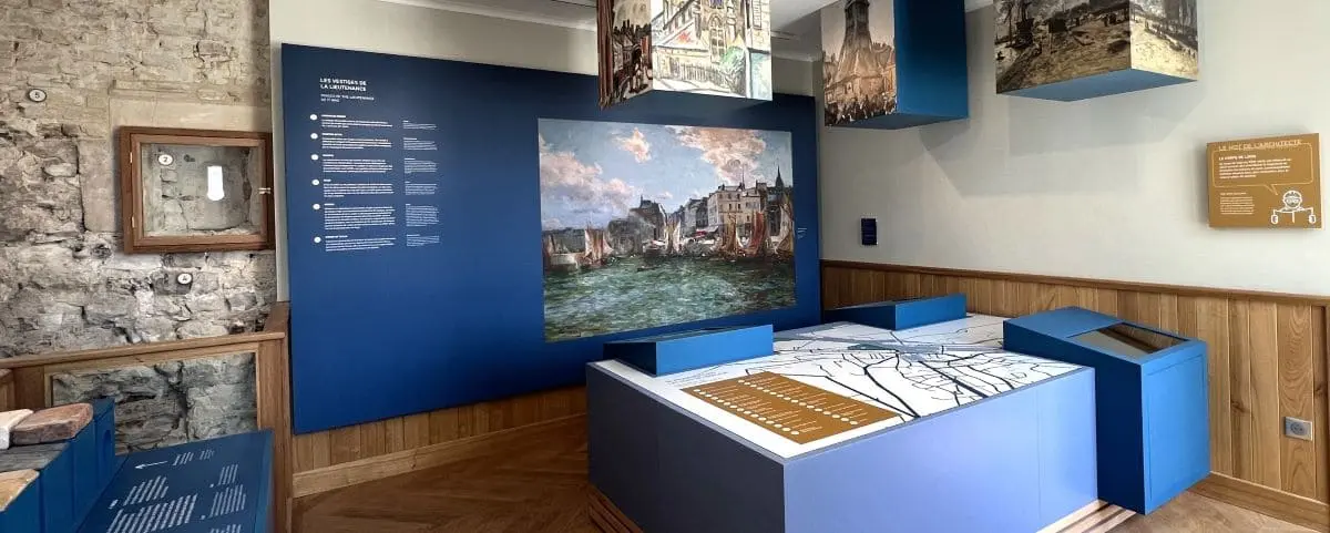 An interior view of a museum exhibit, featuring historical maps and displays about Honfleur. The room is designed with blue and wooden accents, offering an educational experience about the town's maritime history.