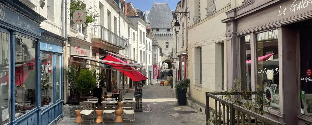 A charming street in the town center of Loches, lined with quaint shops and cafes. Red awnings and outdoor seating create a welcoming atmosphere.