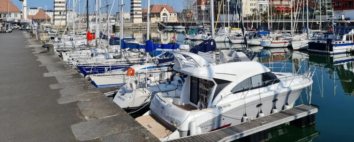 A variety of boats and yachts docked at the marina in Deauville, with the waterfront buildings visible in the background.