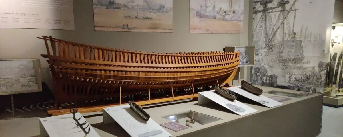 Exhibit at the Maritime Museum on Tatihou Island, featuring a detailed wooden ship model and historical maritime drawings.