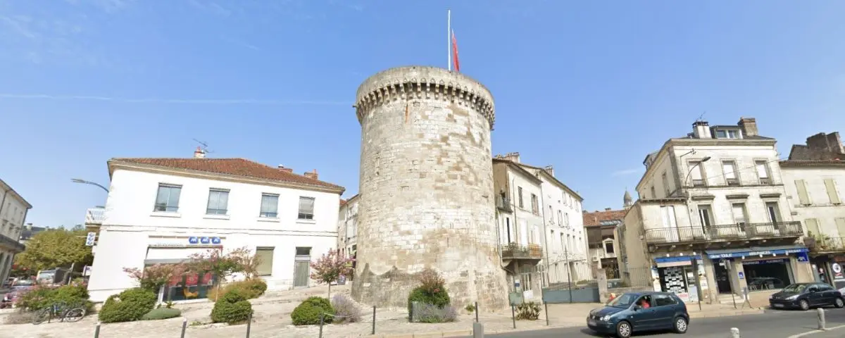 The historic Mataguerre Tower in Périgueux, a circular stone structure with a crenelated top. It stands prominently in a square, surrounded by modern buildings, highlighting its historical significance amid urban development.