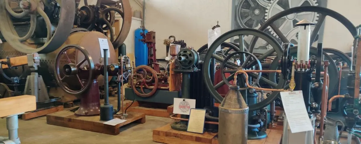 An exhibit at the Mechanical Museum featuring various old engines and mechanical devices. The machinery is arranged in a spacious room, some with informational placards.