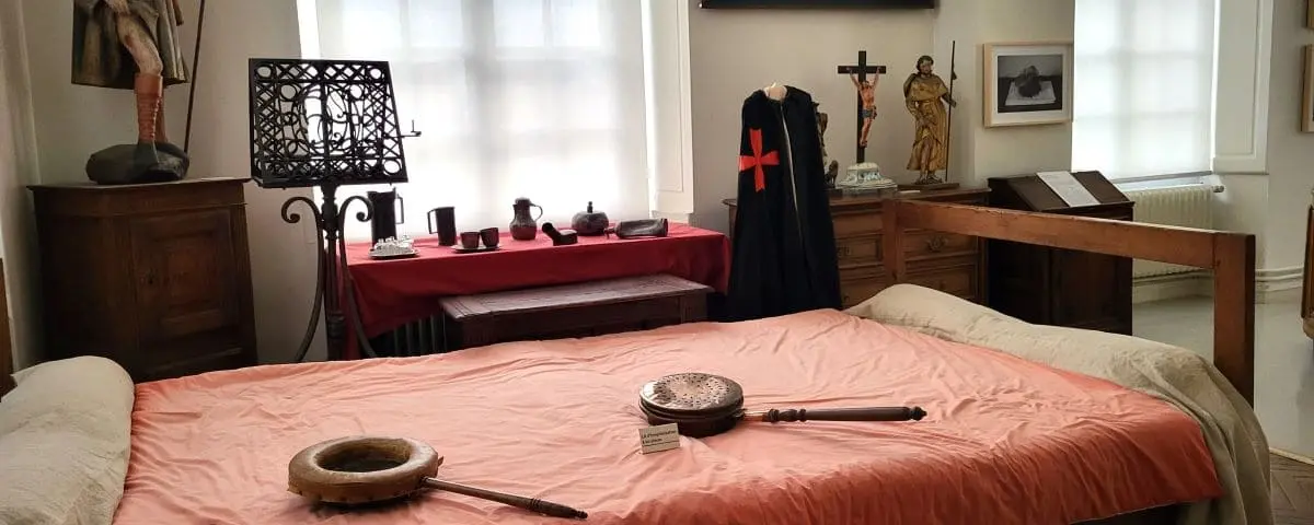 A historical room display at the History of Medicine Museum in Rouen, featuring an old-fashioned bed, religious artifacts, and various medical instruments and uniforms.