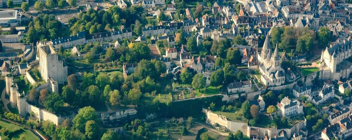 Panoramic aerial view of the medieval city of Loches, featuring dense clusters of historic buildings, winding streets, and the prominent castle and church structures amidst a green landscape.