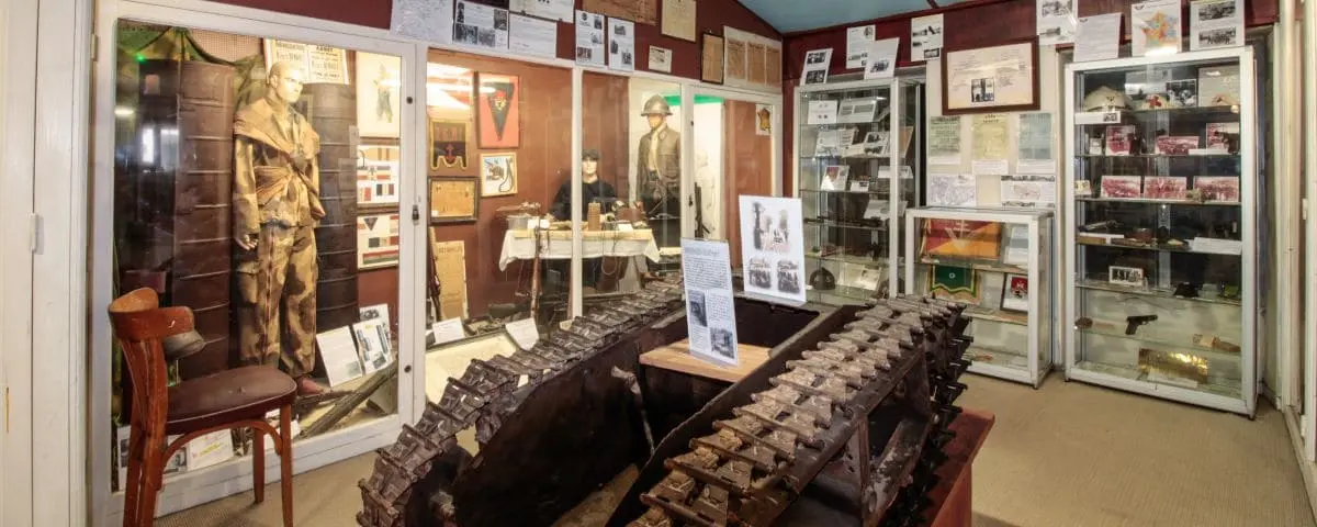 An exhibit in the Military Museum of Périgueux, displaying artifacts and memorabilia. The room includes glass cases with historical items, a large piece of military equipment, and photographs and documents on the walls.