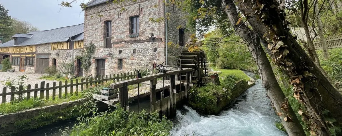 A picturesque scene of an old water mill with a stream flowing rapidly beside it. The building and its surroundings have a rustic charm.