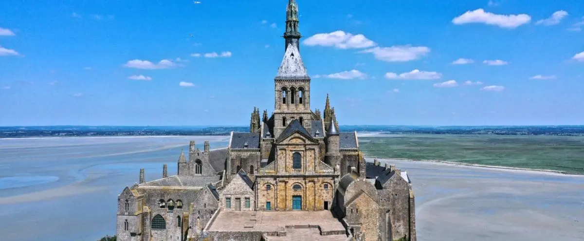 A detailed view of Mont Saint-Michel Abbey, showcasing its gothic architecture with a backdrop of expansive water and land.