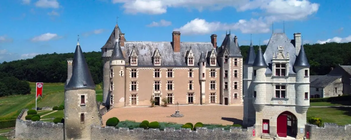 A stunning castle with conical towers and a large central courtyard, surrounded by a green lawn and a bright, sunny sky.