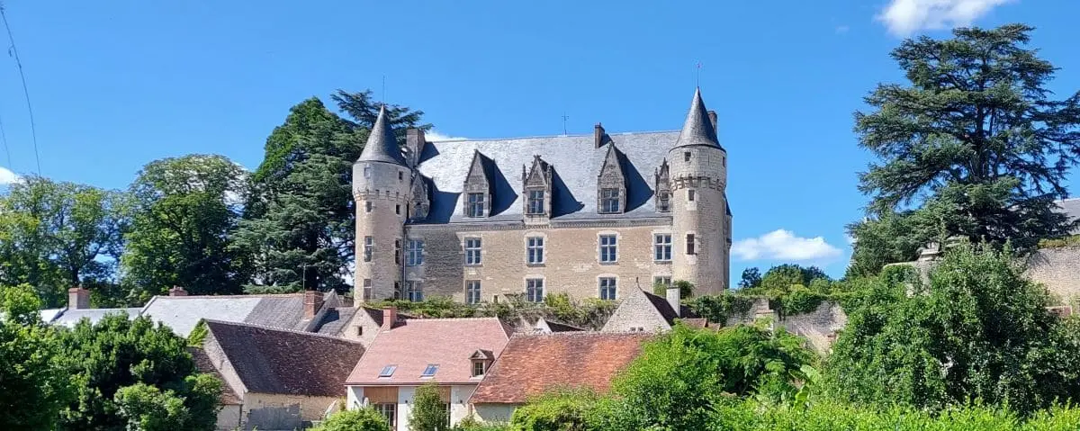 The picturesque Montrésor Castle with its classic towers and stone walls, surrounded by lush greenery and quaint village houses, under a clear blue sky.