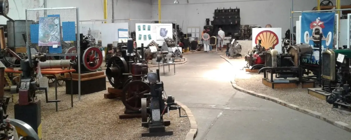 Collection of vintage engines and machinery on display at the Motor Museum in Saumur, arranged in an open exhibition space with informational signs.
