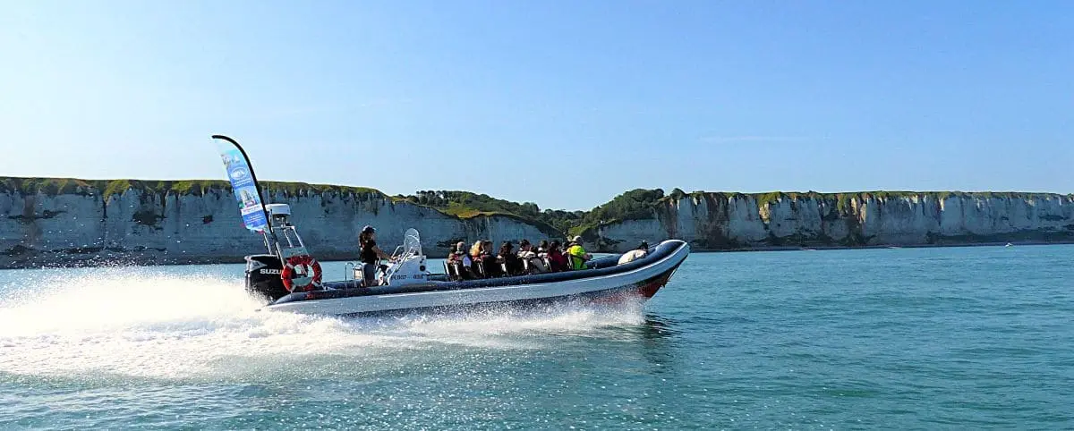 A motorboat speeding along the coast of Fécamp, France, with passengers enjoying the ride and the white cliffs visible in the background.