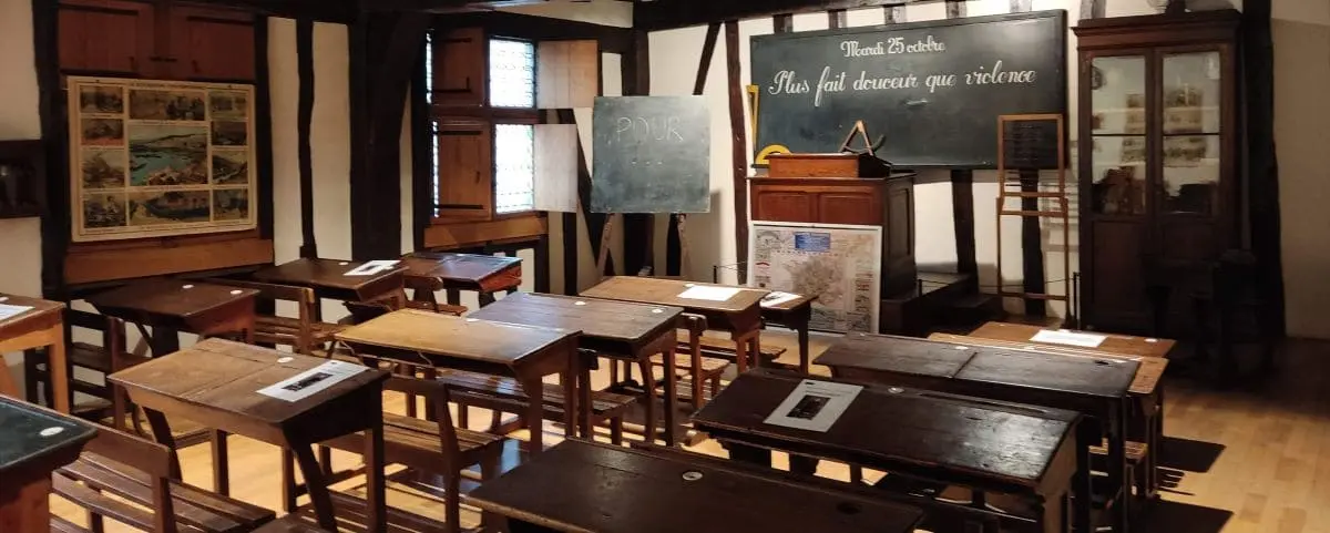 An old-fashioned classroom exhibit at the MUNAE in Rouen, with wooden desks, a chalkboard, and vintage educational posters and materials.