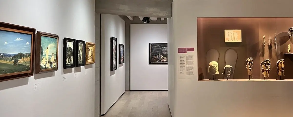 A gallery in the museum at Fontevraud Abbey displaying various paintings on the walls and a glass case with sculptures and artifacts.