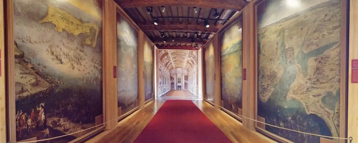 A hallway in the museum in Richelieu lined with large, detailed paintings depicting historical scenes, under warm lighting.
