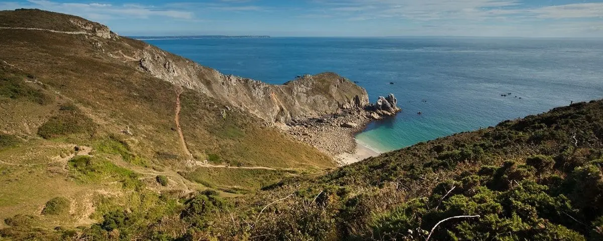 Rugged coastline of Nez de Jobourg with steep cliffs, rocky shoreline, and clear blue water, highlighting the dramatic coastal landscape.