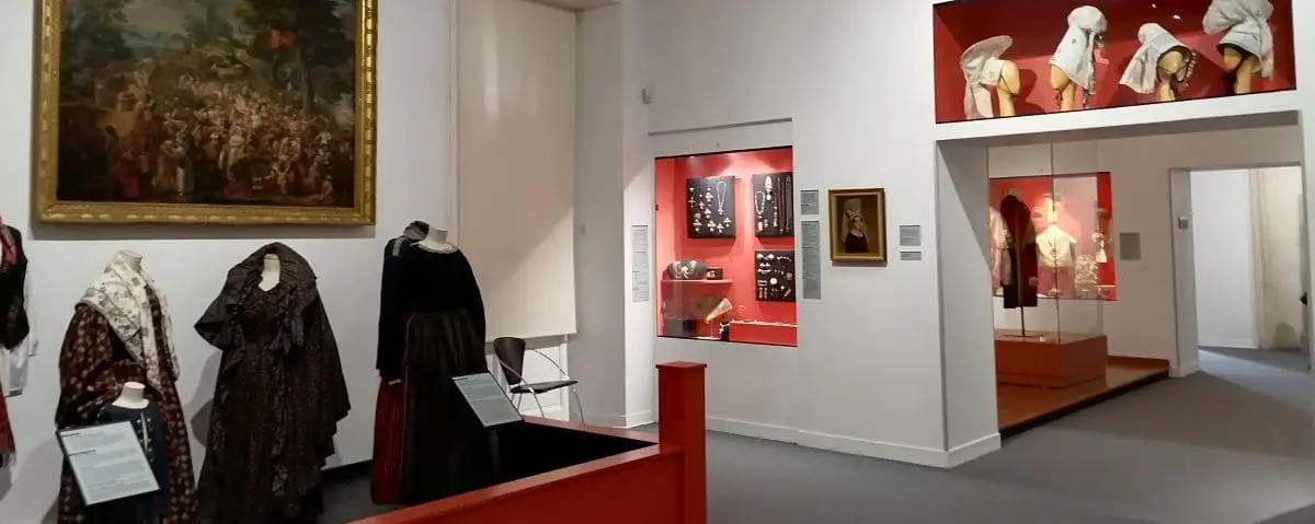 An exhibition room in the Normandy Museum featuring historical clothing and artifacts. Display cases and informative plaques provide context for the exhibits.