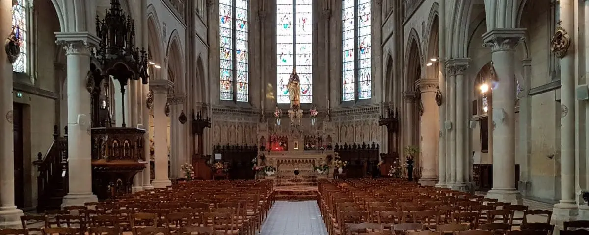 The interior of Notre-Dame-du-Bon-Secours Church in Trouville, showcasing its gothic architecture with stained glass windows, an elaborate altar, and rows of wooden chairs.