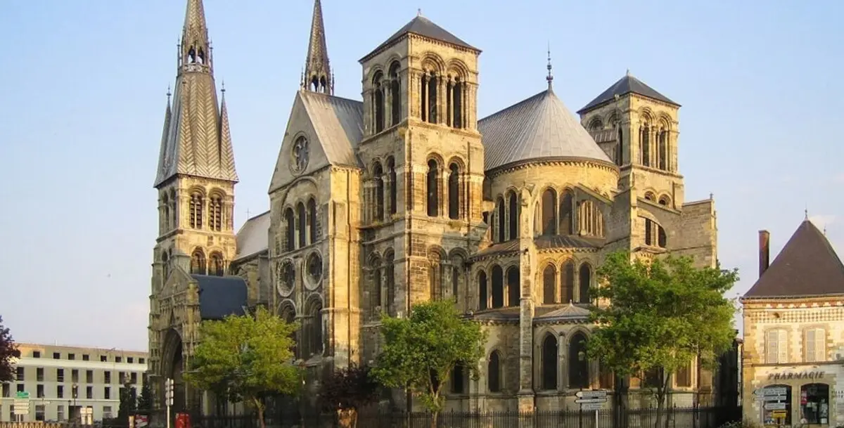 A view of the impressive Notre-Dame-en-Vaux church, showcasing its multiple spires and intricate stone architecture, surrounded by a few trees and adjacent buildings.