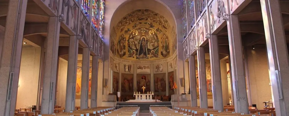 The interior of a basilica with a richly decorated altar, colorful murals, and stained glass windows illuminating the space.