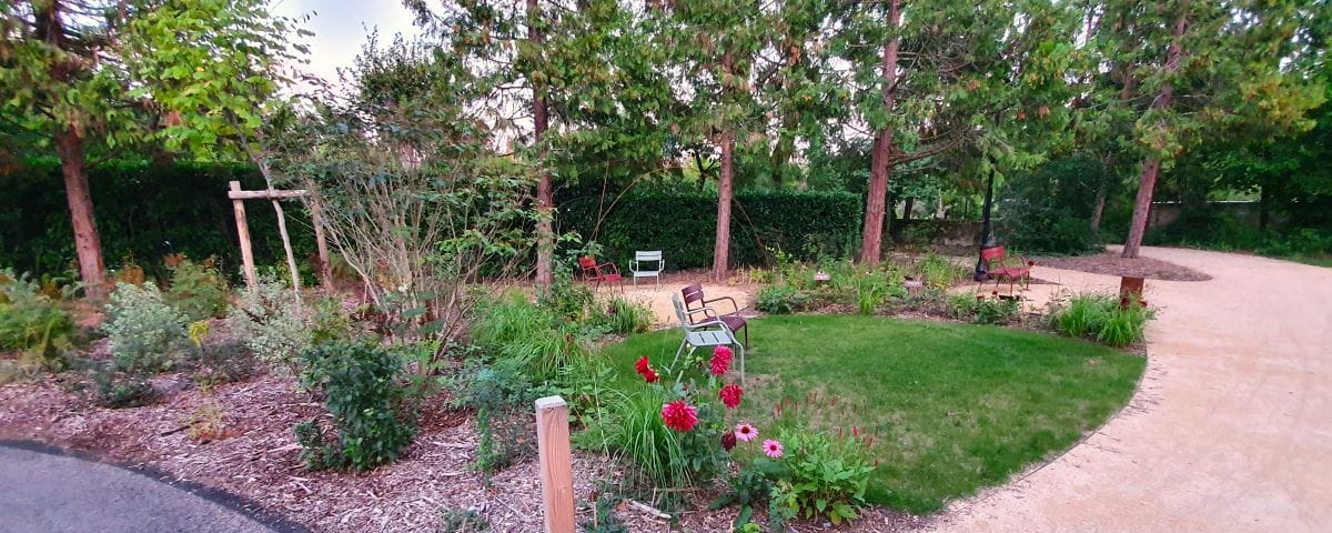 A garden in Chenonceaux featuring a small seating area surrounded by trees and bushes. There are pink flowers, likely peonies (pivoines in French), adding color to the green landscape.