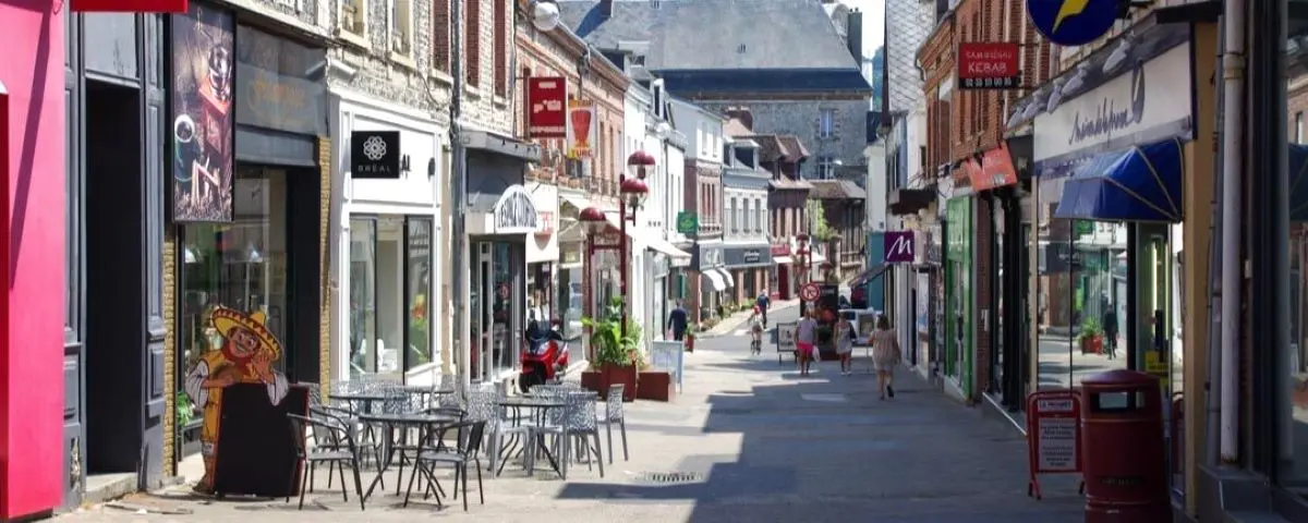 A bustling pedestrian street in Fécamp, lined with shops, cafes, and people strolling along the charming town center.