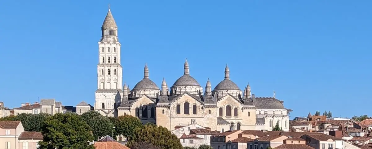 The Périgueux Cathedral, characterized by its distinctive domes and tall bell tower, against a clear blue sky. The impressive architecture stands out amidst the surrounding town buildings, reflecting its religious and cultural importance.