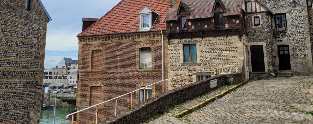 A quaint street in the Pollet district of Dieppe, with cobblestone pathways and historic brick and stone buildings lining the street.