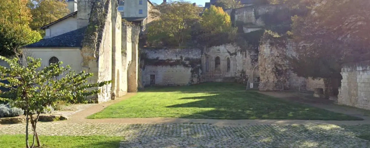 The ruins of Prieuré Nobis in Montreuil-Bellay, with old stone walls and a grassy courtyard, bathed in soft sunlight.