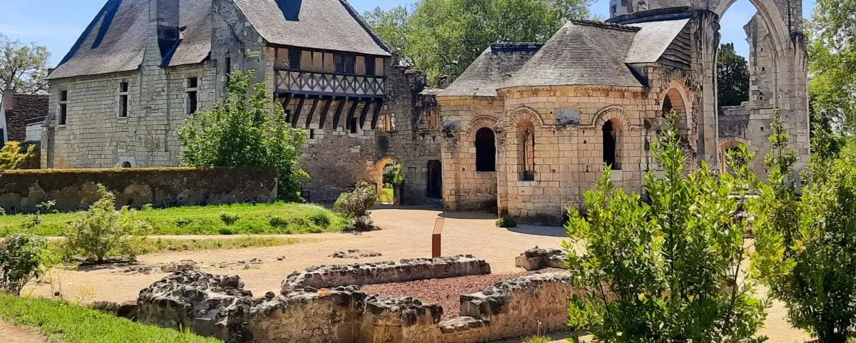 The historical ruins of the Priory Saint Cosme in Tours, France, featuring a mix of well-preserved stone buildings and ancient structures amidst green foliage.