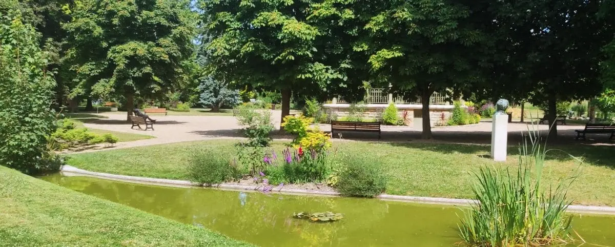 A serene public garden in Loches, showcasing lush greenery, vibrant flowers, and a small pond. Benches are placed throughout the garden for visitors to relax.